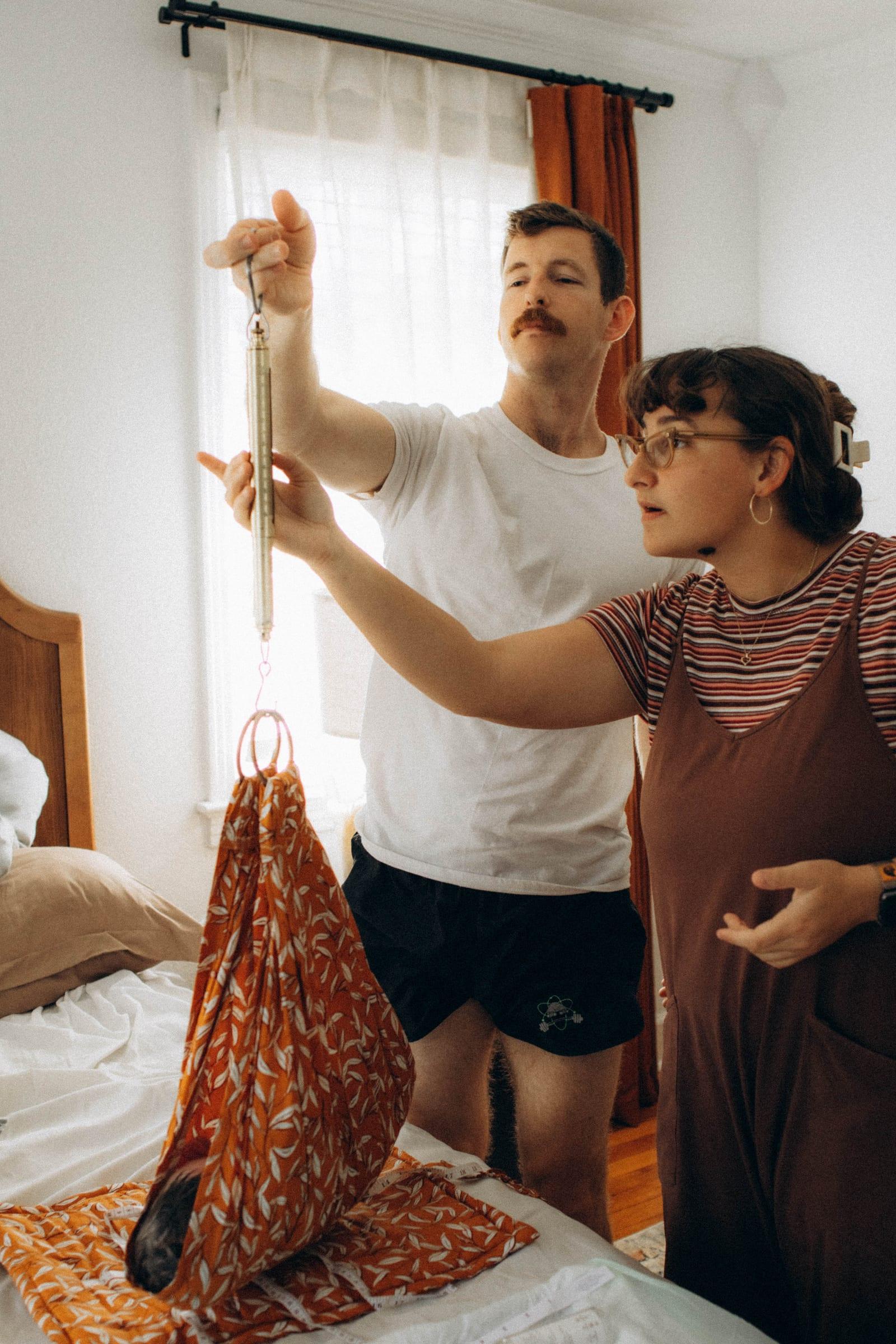 A midwife and a father weighing a newborn in a cloth sling on a hanging scale